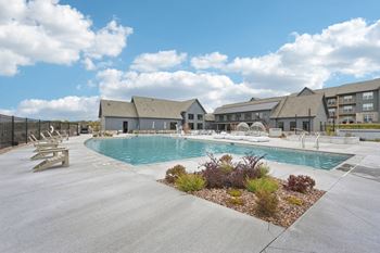 A large outdoor swimming pool surrounded by a concrete patio and a small garden.